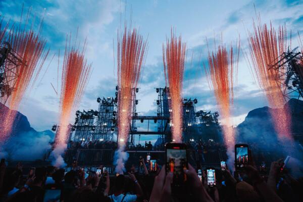 Un concerto emozionante con fuochi d'artificio che esplodono nel cielo. La folla è in visibilio, con molte persone che riprendono il momento con i loro telefoni.