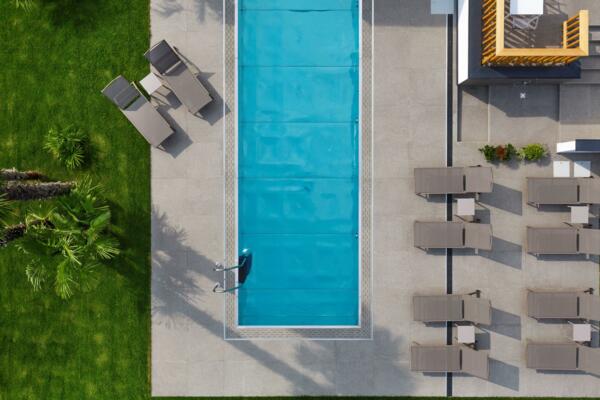 Ein blauer Pool, umgeben von Liegen und einem grünen Rasen. Man sieht auch einige Palmen im Feld.