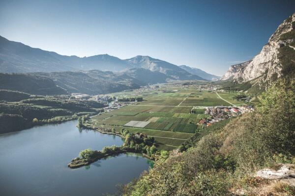 Un paesaggio montano con un lago e terreni agricoli verdi. Le montagne circostanti completano la vista serena e naturale.