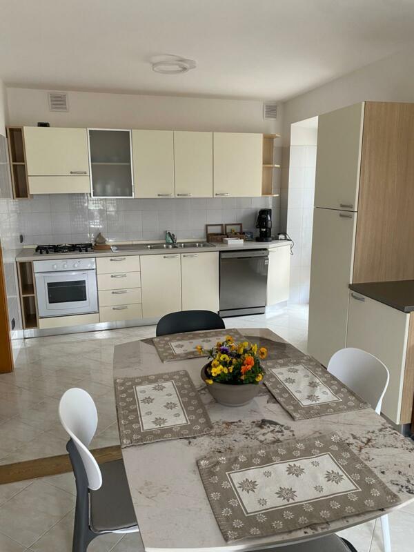 A modern and bright kitchen with light cabinets and an elegant dining table. In the center of the table, there is a vase of colorful flowers.