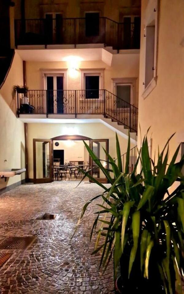 Ein ruhiger Innenhof mit Steinbelag und grünen Pflanzen. Am Ende ist ein Bereich mit Tischen und Stühlen zu sehen.