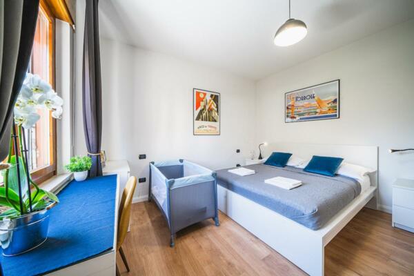Ein helles Zimmer mit einem Doppelbett, einem Kinderbett und modernen Dekorationen. Das Fenster bietet einen Blick auf die umliegende Natur.