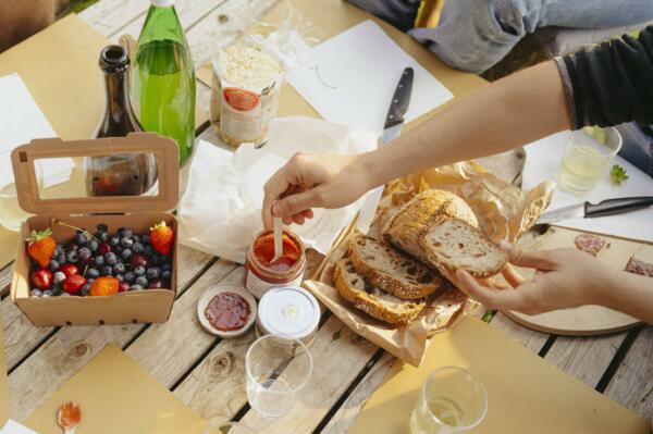 A table set with bread, jam, and fresh fruit. One person is dipping a slice of bread into a bowl of sauce.