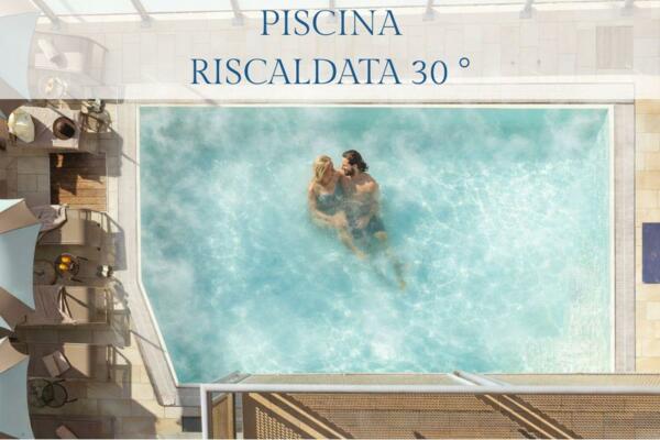 Una piscina riscaldata a 30° con persone che si godono l'acqua. Intorno si vedono sdraio e ombrelloni.
