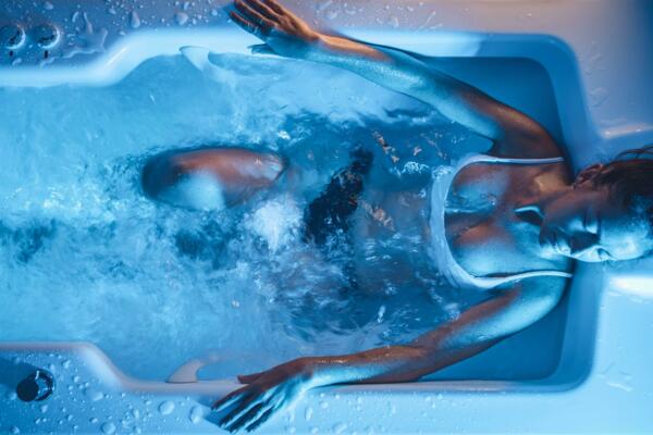 A relaxed woman is in a bathtub full of water. The blue lighting creates a tranquil and rejuvenating atmosphere.