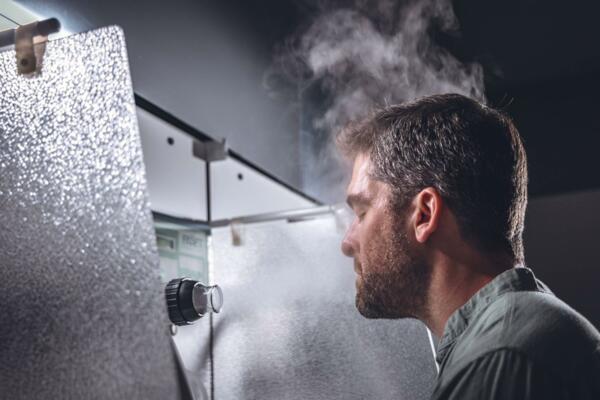 A man approaches a device that emits steam. He is immersed in a professional and technological work environment.