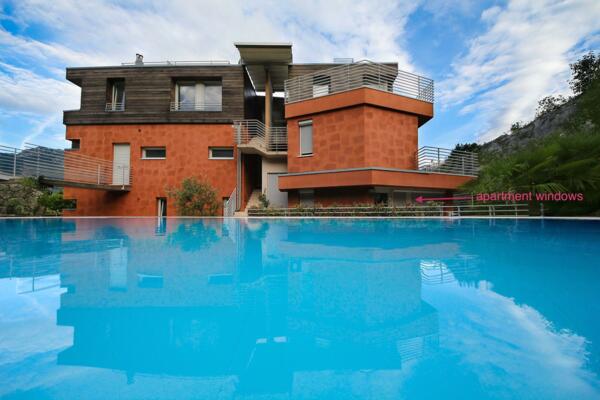 Eine moderne Villa mit Backsteinfassade und großen Fenstern. Der blaue Pool spiegelt den bewölkten Himmel und die elegante Struktur wider.
