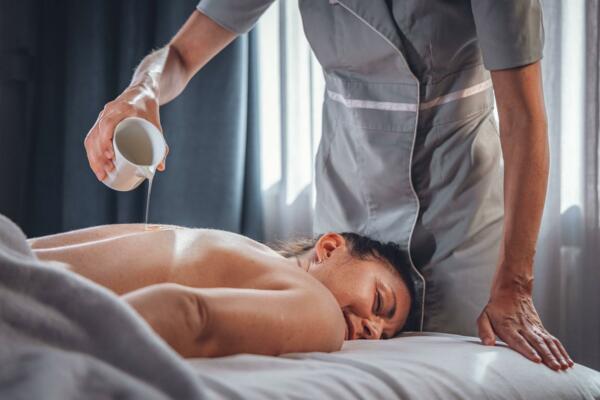 A relaxing massage in a spa, with a therapist pouring oil on a client's back. The soft light creates a calm and serene atmosphere.