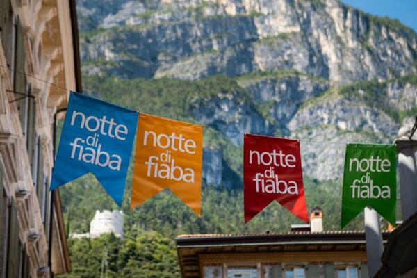 Colored flags are hanging between the buildings, with the words "fairy tale night." In the background, green mountains and a clear sky are visible.