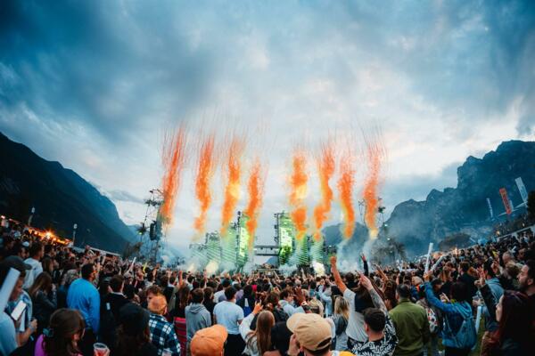 Ein Musikfestival mit einer großen Menge, die live zuhört. Bunte Feuerwerke erleuchten die Bühne und die Berge im Hintergrund.