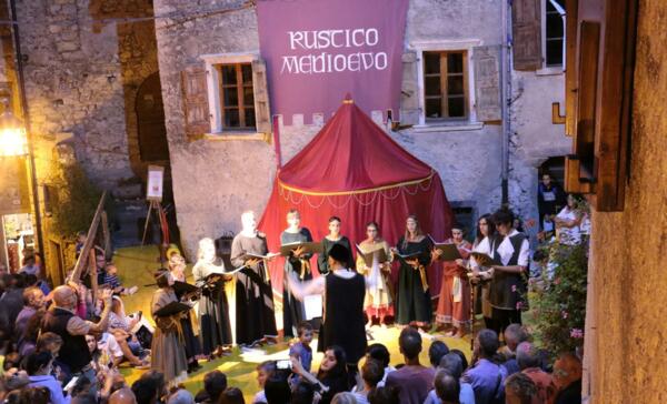 A medieval cultural event with artists performing on an outdoor stage. The scene is crowded with spectators watching with interest.