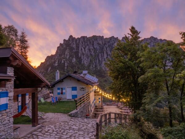 A charming mountain cabin with decorative lights and a spectacular landscape in the background. The sky at sunset displays warm and magnificent color shades.