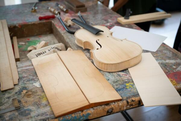Un laboratorio di liuteria con strumenti e pezzi di legno per la costruzione di un violino. Si vedono un violino quasi completato e alcune tavole di legno sagomate.
