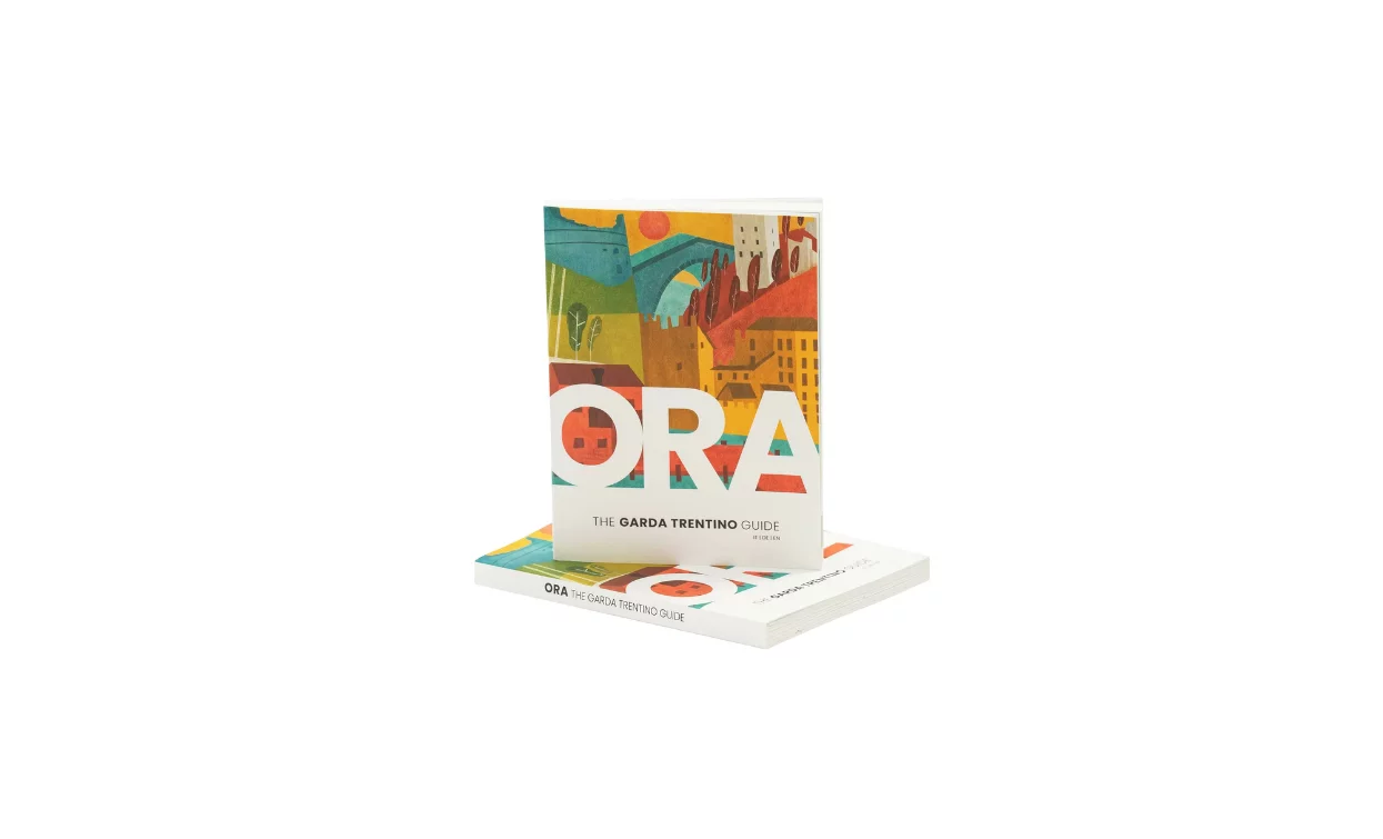 A guide titled "NOW" with a colorful and artistic cover. The guide is dedicated to the Garda Trentino region.