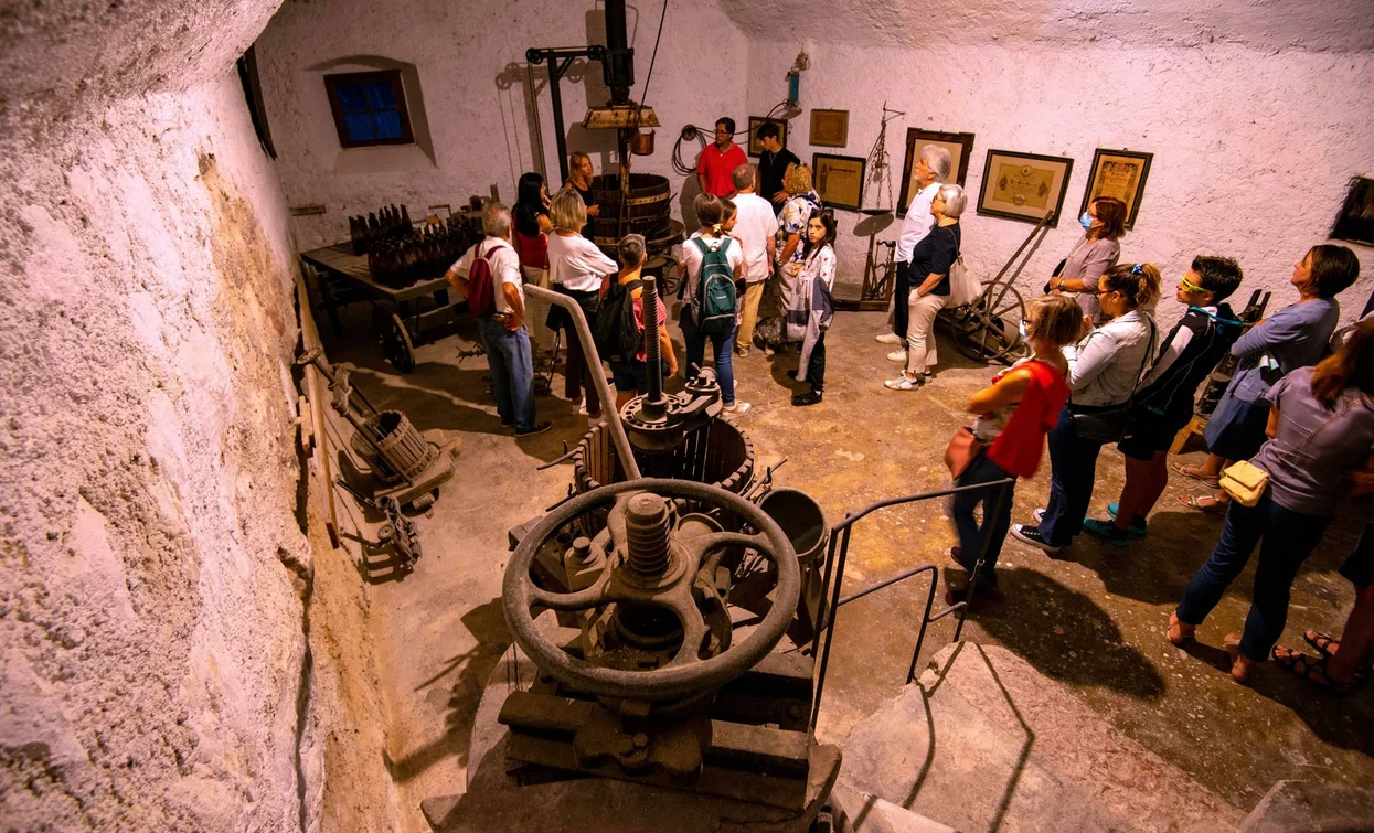 A group of people visiting a museum. You can see historical machinery and stone walls.