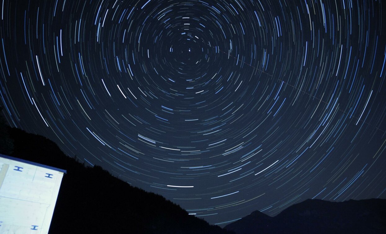 Una scena notturna con stelle in movimento che creano cerchi nel cielo. In primo piano, parte di un paesaggio montano scuro.