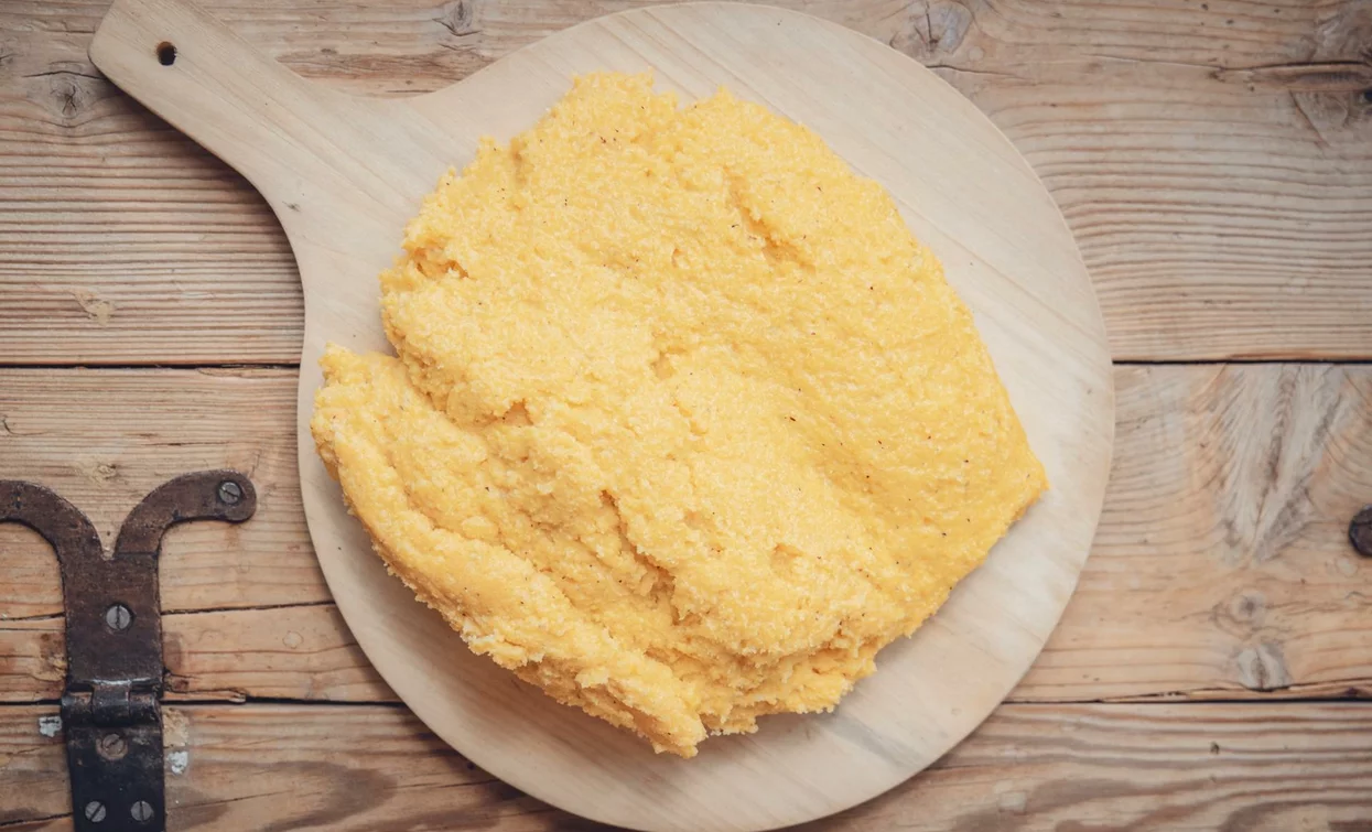 Un morbido impasto di polenta su un tagliere di legno. Il colore giallo brillante rappresenta un alimento tradizionale italiano.