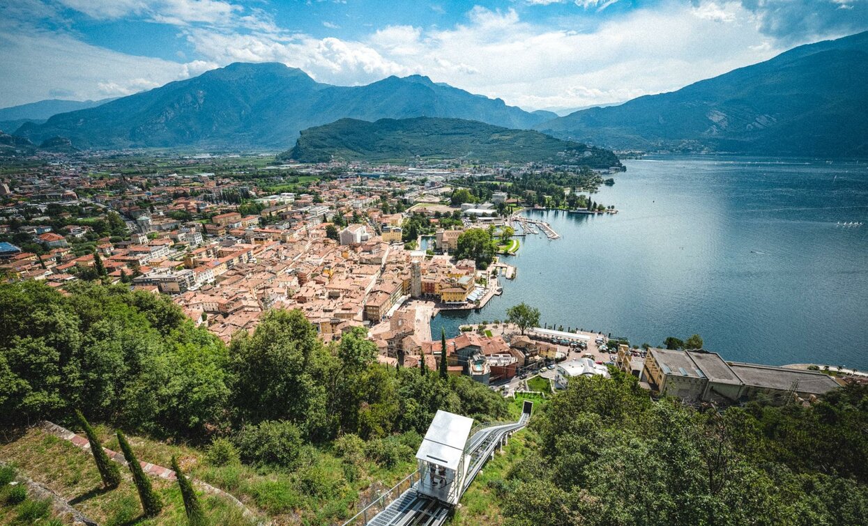 Una vista panoramica di una città situata vicino a un lago, circondata da montagne. Il cielo è sereno e si vedono edifici storici a ridosso dell'acqua.