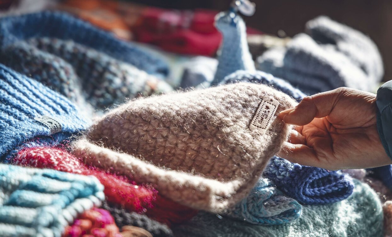 Eine Auswahl an bunten Strickmützen. Eine Hand untersucht eine helle Wollmütze.