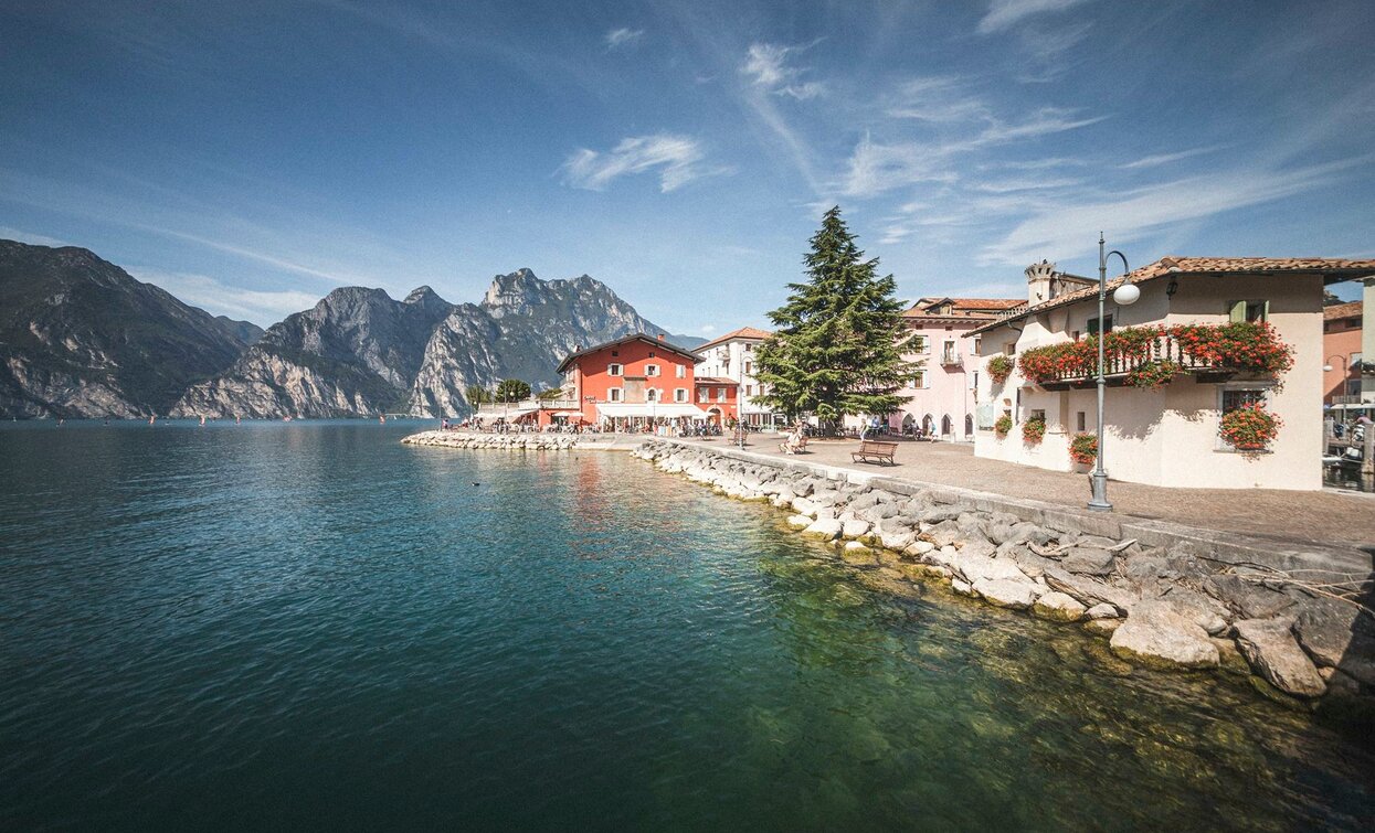 A picturesque lakeside with colorful houses and mountains in the background. The water is clear and calm, creating a serene atmosphere.