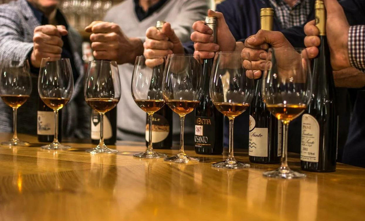 Un gruppo di persone che festeggia, con bottiglie di vino e calici sul tavolo. Le mani si preparano a brindare.